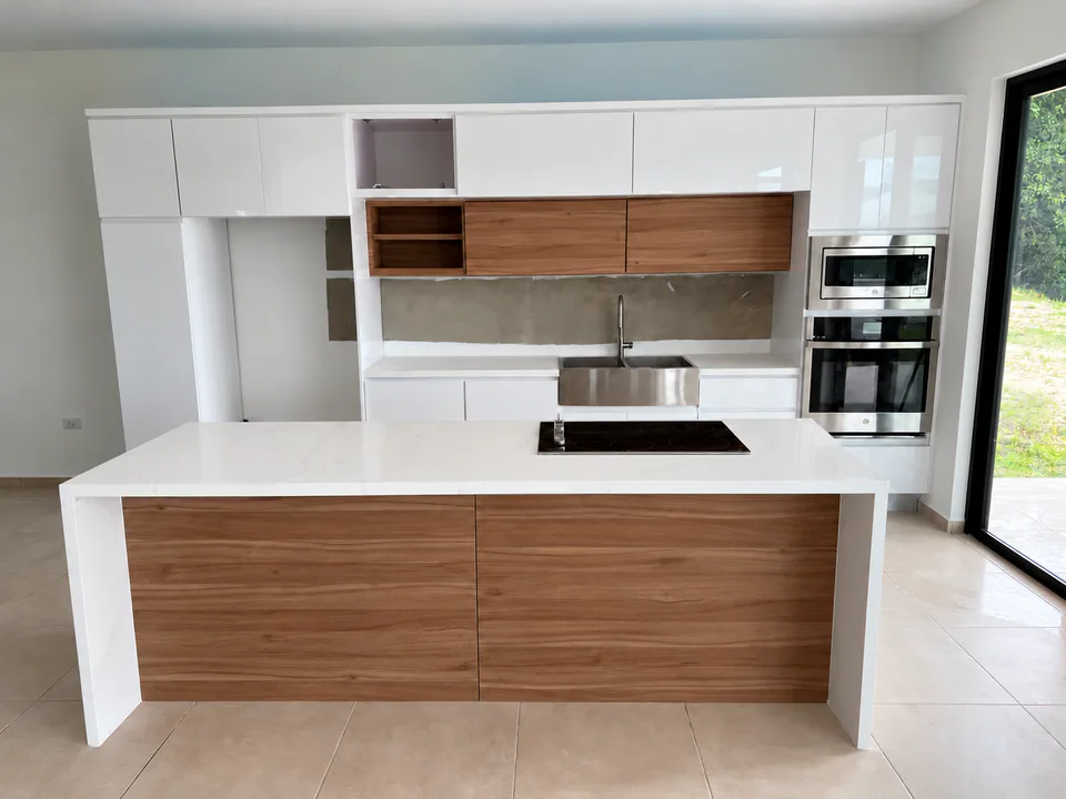 Cocina realizada por M5 con gabinetes blancos, frentes de madera, isla central y electrodomésticos integrados.